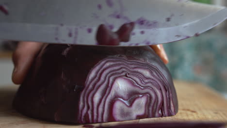 Close-up-woman's-hand-starts-slicing-part-of-purple-red-cabbage-with-a-sharp-knife-in-the-kitchen