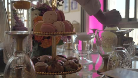 Man-Placing-Carafe-On-Wedding-Table---Macarons-And-Glazed-Choux-On-A-Cake-Stand