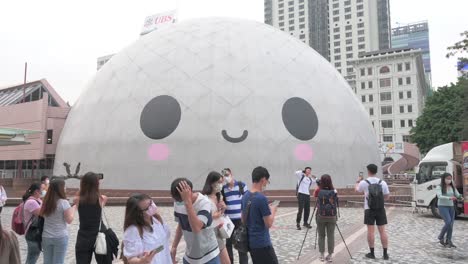 Las-Personas-Toman-Fotos-Y-Selfies-Mientras-Posan-Frente-Al-Museo-Espacial-Mientras-Exhibe-Una-Instalación-De-Arte-De-Cara-Sonriente-En-Su-Superficie-En-Hong-Kong