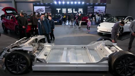 Visitors-look-at-a-Tesla-Motor-chassis-car-and-vehicle-frame-of-a-motor-vehicle,-during-the-International-Motor-Expo-showcasing-EV-electric-cars-in-Hong-Kong