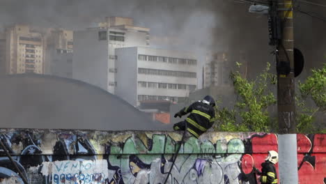 Lone-Sao-Paulo-firefighter-sits-on-concrete-wall-to-suppress-flames,-on-Tereza-Cristina-avenue,-Ipiranga-district