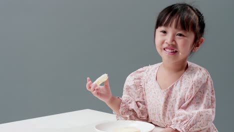 Happy-little-Asian-girl-rubs-her-eyes,-smile,-and-enjoy-eating-crispy-butter-toast-at-home