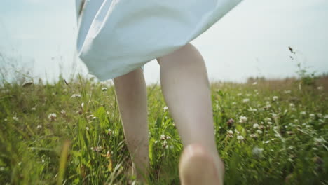 Hippie-woman-running-and-walking-barefoot-in-the-grass-full-of-joy,-tracking-shot-during-a-sunny-day-in-the-outdoors