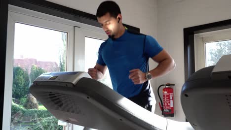 Slow-motion-4K-frontal-shot-of-an-athletic-muscular-man-in-a-blue-T-shirt-running-on-a-treadmill-in-a-gym,-24FPS