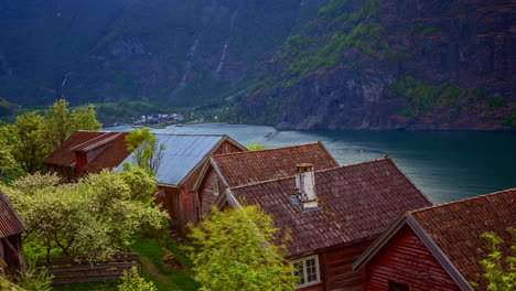 Traditionelle-Norwegische-Häuser-Am-Ufer-Des-Aurlandsfjords-Mit-Vorbeifahrendem-Kreuzfahrtschiff-Im-Hintergrund