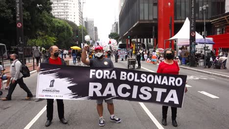 Establishing-shot-of-people-holding-a-banner-saying-"Get-out-racist-Bolsonaro",-on-Paulista-avenue