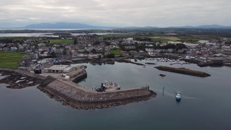 Aerial-view-of-a-fishing-boat-leaving-Ardglass-harbour-on-a-cloudy-day,-County-Down,-Northern-Ireland