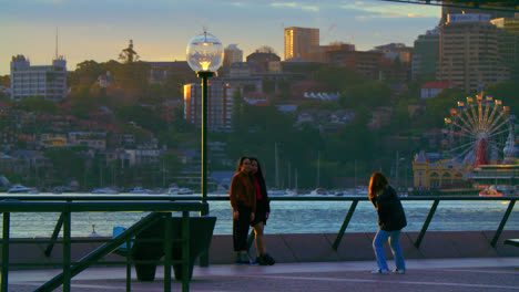 Female-Friends-Taking-Photos-Together-By-The-Sydney-Harbour-Waterfront-In-NSW,-Australia-At-Dusk