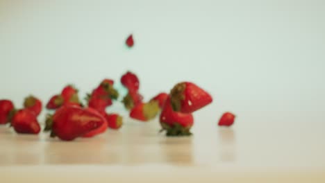 Filmische-Zeitlupenaufnahme-Von-Frischen-Erdbeeren,-Die-Auf-Einen-Tisch-Fallen-Und-Rollen-Und-Abprallen,-Konzept-Für-Gesunde-Ernährung