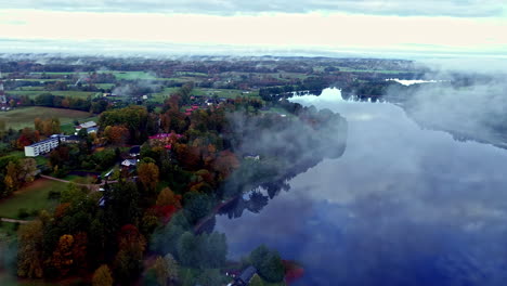 Drone-overview-in-early-morning-with-mist-floating-over-calm-lake-water