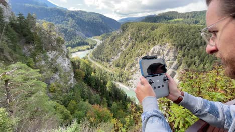 Young-hipster-flying-a-drone-in-a-beautiful-Swiss-mountain-valley-with-river-rhine