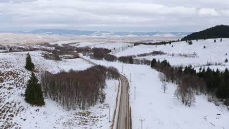 Aerial-view-from-drone-following-road-through-scenic-valley-dusted-in-snow