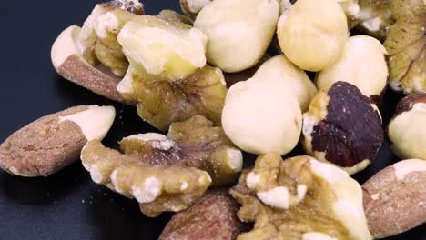 Close-up-detailed-rotating-shot-of-a-trail-mix:-nuts,-walnuts,-almonds-and-hazelnuts-mix-macro-shot,-close-up-shot-rotating-over-a-black-surface-background