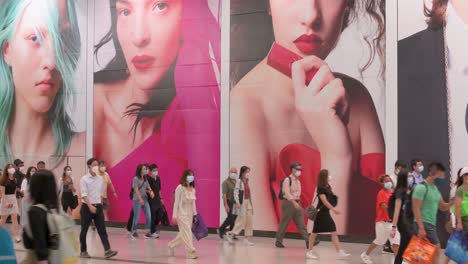 Large-crowds-of-people-are-seen-walking-past-a-large-commercial-advertisement-banner-at-Hong-Kong-MTR-subway-station-early-morning-in-Central-district,-Hong-Kong