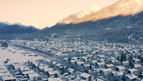 Snowy-Garmisch-Partenkirchen-town-below-sunlit-mountains,-drone-shot