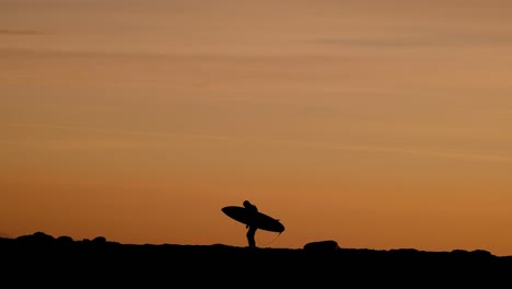Surfer-silhouette-at-sunset-walking-over-rocks