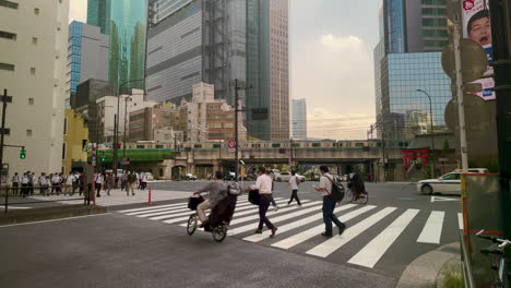 Menschenmenge-In-Tokio-überquert-Die-Straße,-Im-Hintergrund-Fährt-Eine-Hochbahn-Vorbei