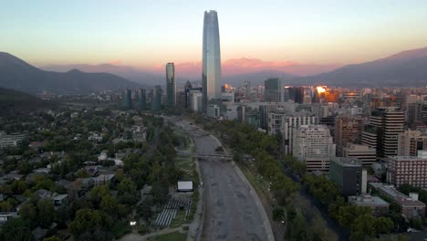 Aerial-parallax-of-open-air-free-cinema,-Mapocho-river,-Sanhattan-skyscraper-and-hills-in-background-at-blue-hour-in-Providencia,-Santiago,-Chile
