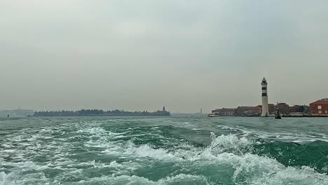 Low-angle-water-surface-pov-of-Murano-lighthouse-in-Venice-lagoon-seen-from-ferry-boat,-Italy