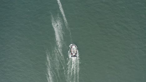 Overhead-aerial-drone-footage-of-a-fishing-boat-in-ocean-water,-going-out-to-see,-sunny-day