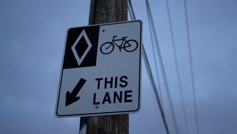 HOV-bike-lane-diamond-sign-on-wooden-post-in-urban-area-with-exposed-telephone-wires-and-electricity-lines---sign-for-bikers,-cyclists,-and-bicyclists---road-rules-and-signs-for-bicycles-on-cloudy-day