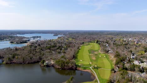 Huge-golf-course-field-near-small-town-and-Atlantic-ocean,-aerial-pan-left-view
