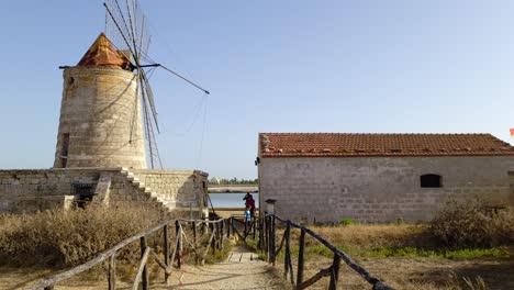 Slow-motion-of-family-of-tourists-at-Mulino-Maria-Stella-windmill-in-front-of-saline-of-Paceco,-Sicily