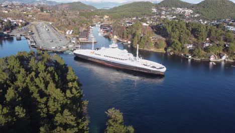 Hybrid-powered-ferry-Flatoy-is-departing-port-of-Halhjem-along-road-E39-on-Norway-western-coast---Beautiful-sunny-day-aerial-with-trees-in-foreground-ferry-in-middle-and-pier-in-background