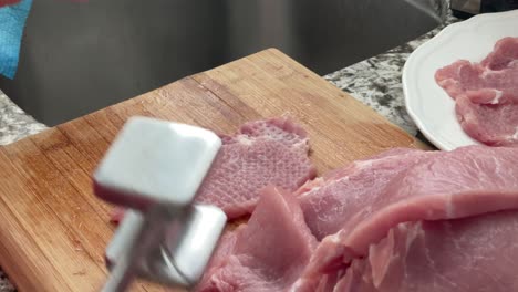 Tenderizing-pork-with-meat-mallet-tool---using-meat-tenderizer-meat-pounder-to-prepare-slabs-of-pork-and-seasoning-with-salt-for-por-schnitzels-recipe-at-home-in-kitchen-slow-motion-slo-mo