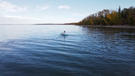 Woman-kayaking-on-a-large-blue-lake-in-front-of-autumn-foliage-in-Alberta,-Canada