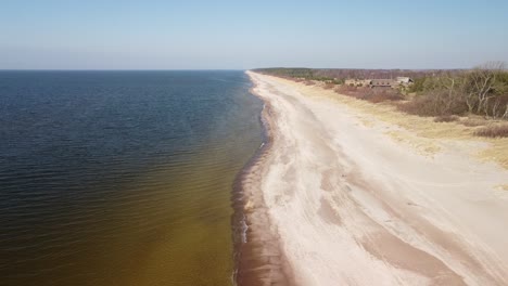 Aerial-view-of-sea-waves-crashing-into-the-beach-with-white-sand-on-a-sunny-spring-day,-Baltic-sea,-Pape-beach,-Latvia,-wide-angle-revealing-drone-shot-moving-backwards-camera-tilt-up