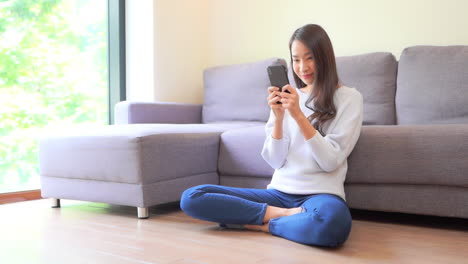 Junge-Hübsche-Asiatische-Frau,-Die-In-Der-Privatsphäre-Ihres-Zuhauses-Textnachrichten-Auf-Dem-Smartphone-Liest