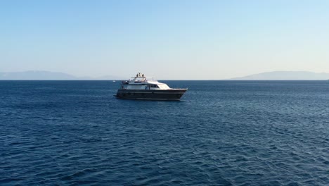 Luftdrohne-Umkreist-An-Einem-Sonnigen-Sommertag-Eine-Schwarz-weiße-Yacht,-Die-Im-Blauen-Wasser-Des-Ägäischen-Meeres-Zwischen-Der-Türkei-Und-Griechenland-Verankert-Ist