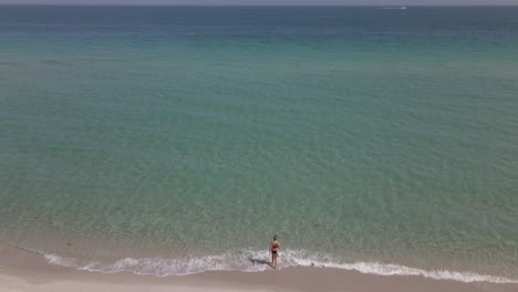 Young-Caucasian-woman-in-bikini-walks-on-sandy-beach-toward-warm-water