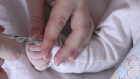 Caring-mom-cutting-baby-nails-on-tiny-baby's-thumb,-close-up