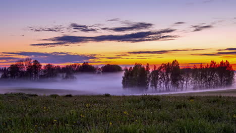 Scenic-vibrant-sunset-time-lapse-of-mist-flowing-over-farm-land,-vivid-sky