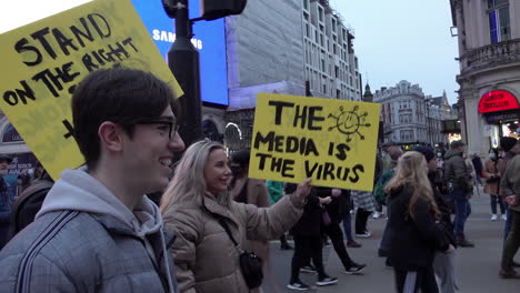 A-woman-holds-a-handmade-yellow-placard-that-says,-“The-media-is-the-virus”-during-a-protest-opposing-mandatory-Covid-vaccines-and-vaccine-passports