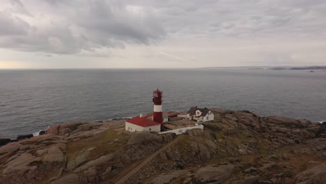 Ryvingen-lighthouse-at-sunset---Red-and-white-lighthouse-on-small-island-at-southernmost-point-of-Norway---Aerial-with-north-sea-and-dramatic-sky-background