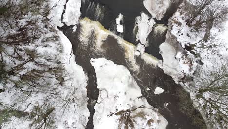 Aerial-top-down-drone-view-of-a-flowing-stream-in-winter-with-snow-covering-the-land-around-it