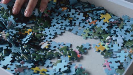 Woman-hand-browsing-through-colorful-jigsaw-puzzle-game-pieces-slow-motion-50i