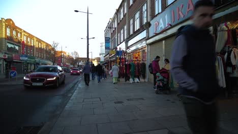 Pedestrians-Walking-Along-Pavement-In-Southall-With-Traffic-Going-Past-In-Late-Afternoon-On-16-January-2022