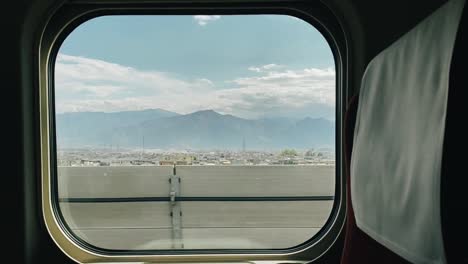 View-of-a-city-with-mountains-in-the-background-on-a-sunny-day-from-a-train-window-while-going-fast