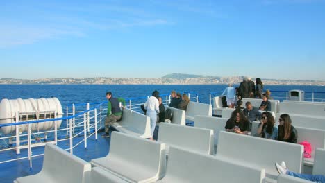 Vista-De-Los-Turistas-Sentados-En-El-Banco-Blanco-En-Un-Barco-Turístico-Mientras-Viajan-De-Nápoles-A-Capri-En-Un-Día-Soleado