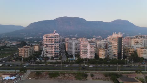 Luftdrohnenaufnahme-Einer-Reihe-Von-Wohngebäuden-Und-Hotels-Am-Meer-In-Alanya,-Türkei,-Mit-Blick-Auf-Die-Bergkette-Im-Hintergrund