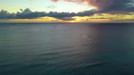 Sailboats-Traveling-Across-the-Pacific-Ocean-on-Tourist-Vacation-in-a-Hawaiian-Sunset,-Sailing-The-Waves-Off-the-Coast-of-Waikiki-Beach-In-Honolulu---Aerial-Drone-Flyover