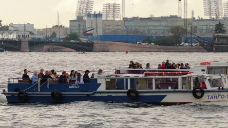 Tourists-On-A-Ferry-Boat-Sailing-On-The-Neva-River-With-The-Cityscape-Of-Saint-Petersburg-In-Russia