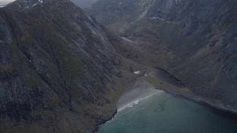 Aerial-view-approaching-a-beach-between-mountains-in-Lofoten,-Norway---tilt,-drone-shot