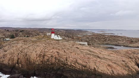 Low-altitude-aerial-around-Lindesnes-lighthouse-with-tourists-walking-around-museum-buildings---Dramatic-clouds-and-north-sea-background---Southern-Norway