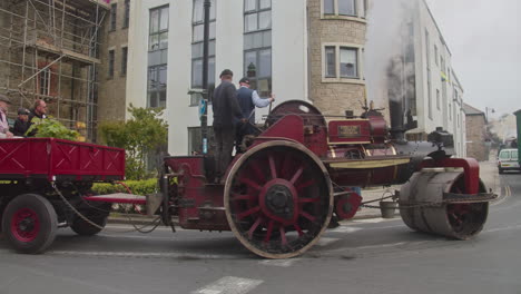 Two-Men-Drive-Steam-powered-Road-Roller-With-Trailer-In-The-Street-During-TheTrevithick-Day-In-Camborne,-England,-UK
