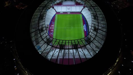 Vista-Aérea-Sobre-El-Moderno-Estadio-Oficial-De-Fútbol-Del-Club-West-Ham-United-Club-Arena-Por-La-Noche-Inclinado-Hacia-Abajo-Birdseye